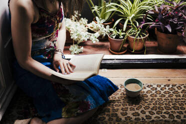 Woman reading book while sitting on floor at home - EBBF00297