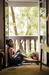 Frau genießt Kaffee, während sie auf dem Balkon zu Hause sitzt - EBBF00302