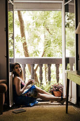 Woman enjoying coffee while sitting by balcony at home - EBBF00302