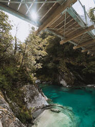 Schmale Holzbrücke über einen beeindruckenden Bergfluss an einem sonnigen Tag in Blue Pools, Neuseeland - ADSF00001