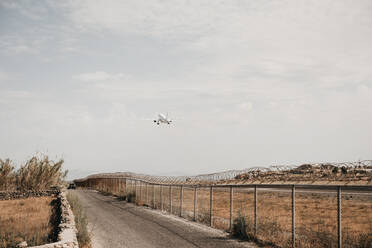 Rückansicht eines Flugzeugs, das vom Flughafen aufsteigt, umschlossen von einem Sicherheitsdraht in der Nähe einer Straße mit Auto in Mykonos - ADSF00025