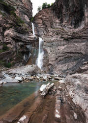 Hohe steile Klippe mit kleinem Kaskadenwasserfall, der in einen reinen Fluss mündet - ADSF00033