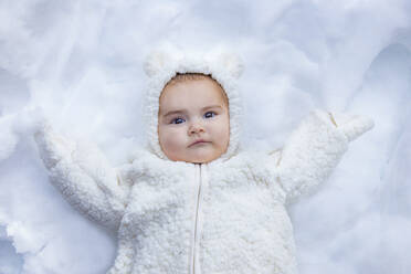 Von oben aufgenommenes süßes Baby in warmer Kleidung, das auf weißem Schnee liegt und in die Kamera schaut - ADSF00052