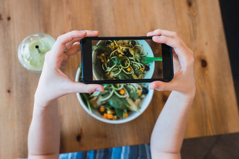 Crop Shot von oben einer Frau, die ein Smartphone benutzt und einen Salat auf dem Tisch fotografiert - ADSF00083