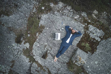 Aerial view of businessman wearing suit with hands behind head relaxing on land in forest - HMEF00993