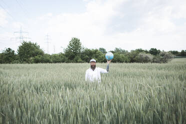 Bärtiger Mann hält Globus, während er inmitten eines Kornfelds vor dem Himmel steht - HMEF01009