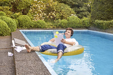 Young man sitting on airbed in swimmingpool and working - UKOF00002