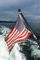 USA, Washington, amerikanische Flagge auf dem Rücken eines fahrenden Motorboots - RUNF03705