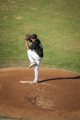 Teenager-Baseballspieler in schwarz-weißer Uniform in voller Montur auf dem Mound - CAVF86218