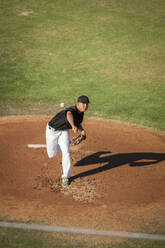 Jugendlicher Baseballspieler in schwarz-weißer Uniform beim Werfen - CAVF86220