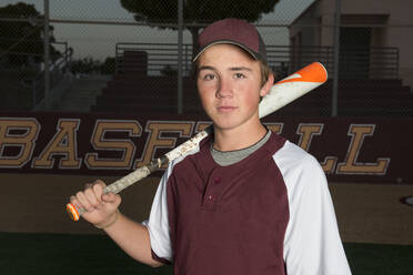Porträt eines High-School-Baseballspielers in kastanienbrauner Uniform, der seinen Schläger hält - CAVF86255