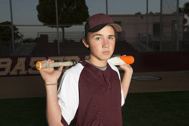 Porträt eines High-School-Baseballspielers in kastanienbrauner Uniform, der seinen Schläger hält - CAVF86261