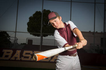 Portrait eines High School Baseballspielers in kastanienbrauner Uniform, der seinen Schläger schwingt - CAVF86262