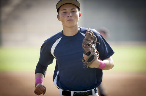 Nahaufnahme eines jugendlichen Baseballspielers in blauer Uniform, der vom Feld joggt - CAVF86272