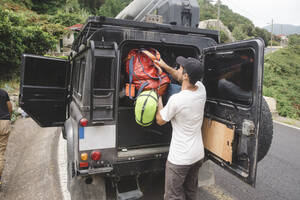 Bergsteiger packt Rucksack in den Kofferraum eines Autos - CAVF86335