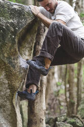 Full body of a male rock climber climbing a rock in a forest - CAVF86352