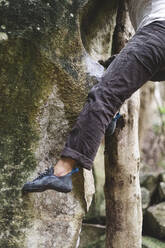Lower part of a male climber climbing at rock in the forest - CAVF86355