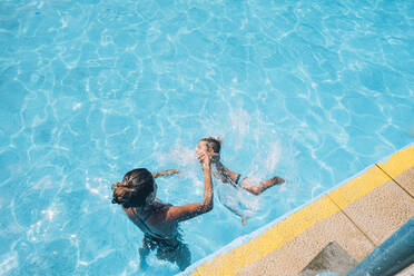 Woman helping her child to jump into the pool - CAVF86364