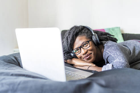 Junge Frau mit Laptop, die zu Hause auf dem Bett einen Film ansieht - MEUF01049
