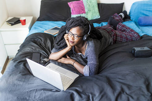 Junge Frau mit Laptop, die zu Hause auf dem Bett einen Film ansieht - MEUF01050