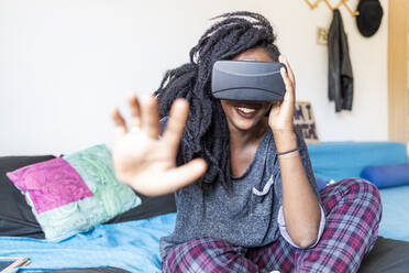 Junge Frau mit Virtual-Reality-Brille auf dem Bett sitzend - MEUF01056