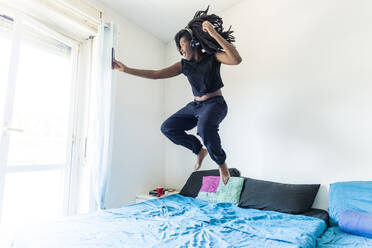 Young woman using smartphone and listening music jumping on bed - MEUF01074