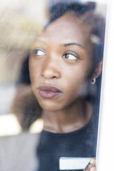 Porträt einer jungen Frau mit Dreadlocks, die aus dem Fenster schaut - MEUF01077