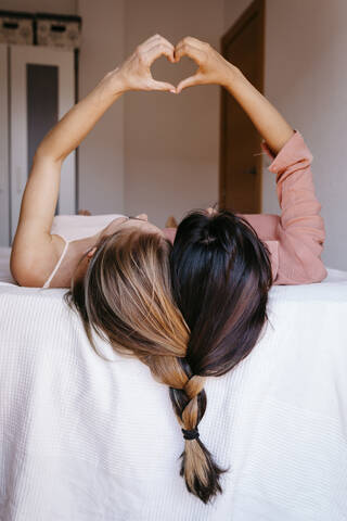 Freunde machen Herzform mit Händen, während sie auf dem Bett liegen, lizenzfreies Stockfoto