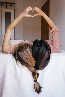 Friends making heart shape with hands while lying on bed - TCEF00802