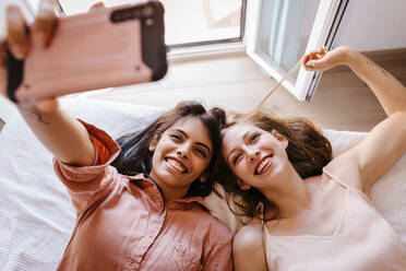 Freunde machen ein Selfie mit dem Handy, während sie zu Hause auf dem Bett liegen - TCEF00805