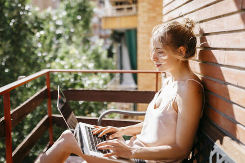 Young woman working on laptop in balcony - TCEF00810