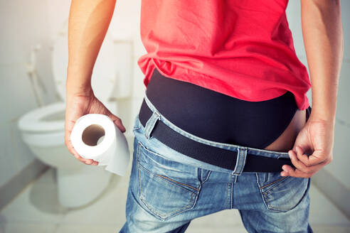 Midsection of Man With Toilet Paper Standing In Bathroom - EYF08885