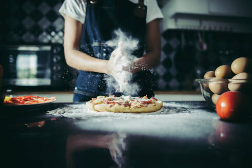 Mittelteil einer Frau bei der Zubereitung von Pizza in der Küche zu Hause - EYF08920