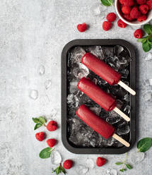 Raspberry popsicles on a tray with ice and fruit on grey background. - CAVF86376