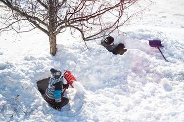 Zwei Jungen bauen an einem sonnigen Wintertag Schneeburgen mit Schaufeln. - CAVF86403