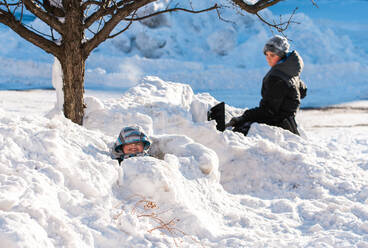 Zwei Jungen bauen an einem sonnigen Wintertag Schneeburgen mit Schaufeln. - CAVF86404