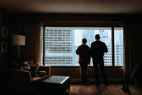 Mann und Junge blicken aus dem Fenster auf die hohen Gebäude der Stadt draußen. - CAVF86407