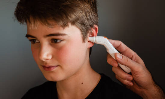 Tween boy getting temperature taken with an ear thermometer. - CAVF86419