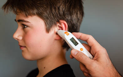 Ein kleiner Junge, der mit einem Ohrthermometer Fieber misst. - CAVF86420