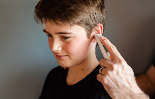 Tween boy getting temperature taken with an ear thermometer. - CAVF86422