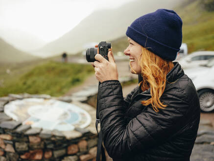 Frau beim Fotografieren der Three Sisters of Glencoe an einem regnerischen Tag - CAVF86440