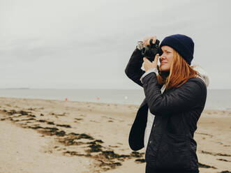 Woman taking photos on beach in Scotland - CAVF86488