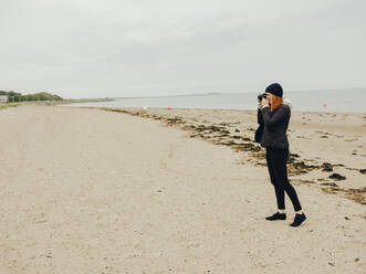 Woman taking photos on beach in Scotland - CAVF86489