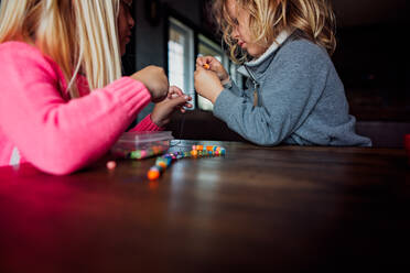 Kleiner Junge und Mädchen machen Perlenkette innen an einem Tisch - CAVF86493