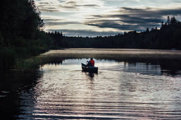 Man casting fishing line in lake with friend sitting in rowboat stock photo