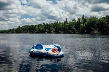 Young child laying on floating raft on river in northern ontario - CAVF86519
