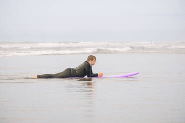 Boy lying on a surfboard on the sand at the beach - CAVF86522
