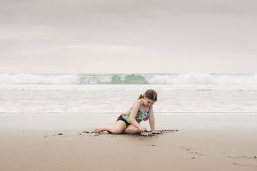 Junges Mädchen sitzt und spielt am Strand - CAVF86525