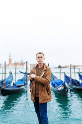 Junger blonder Mann in einer braunen Jacke mitten auf den Straßen von Venedig - CAVF86527