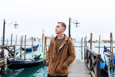 Junger blonder Mann in einer braunen Jacke mitten auf den Straßen von Venedig - CAVF86528